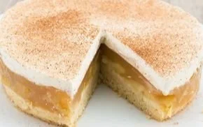 Apfel-Sahne-Torte auf einem weißen Teller mit frischen Äpfeln und Sahne