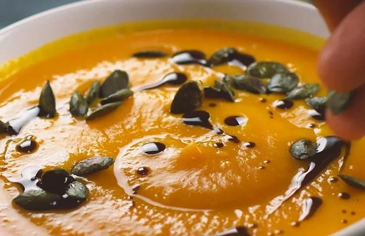 Cremige Kürbis-Möhren-Suppe in einer Schüssel mit frischen Zutaten